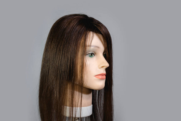 Side view of a mannequin head wearing a brunette wig or toupee. - Photo, Image
