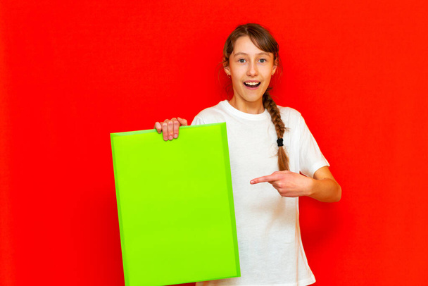 Front view teenager girl showing blank paper.Mock up,banner,copy space.Bright red studio background. - Photo, Image