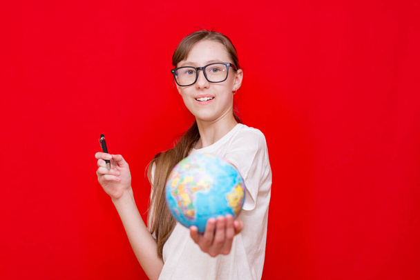Close up teenager girl holding earth globe eyewear pen on red studio background - 写真・画像