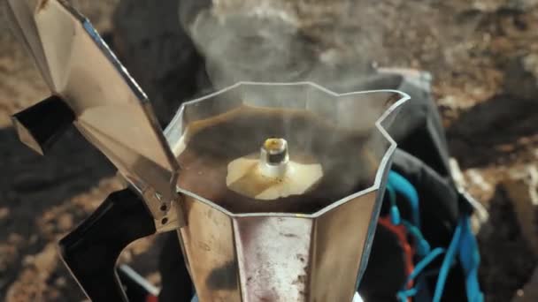 Una caffettiera su un fornello a gas portatile, vista dall'alto. Il caffè comincia a bollire e riempie il contenitore della caffettiera. Fare il caffè durante un'escursione - Filmati, video