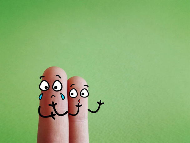 Zwei Finger sind als zwei Personen dekoriert. Einer von ihnen weint. - Foto, Bild
