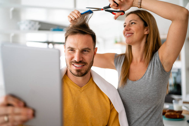 Couple having hair cut at home during isolation coronavirus pandemic, online hairdressing learning on a tablet - Photo, Image