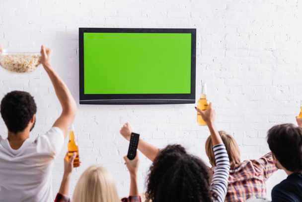 vista posterior de amigos multiculturales viendo la competición deportiva en la televisión en primer plano borrosa - Foto, imagen