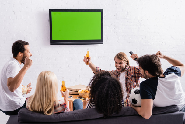 excited multicultural football fans showing success gesture and holding beer near led tv on wall - Fotoğraf, Görsel