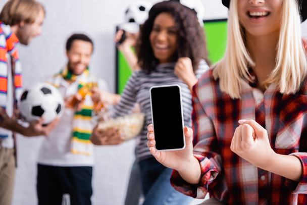 smiling woman showing win gesture while holding smartphone with blank screen near multicultural friends on blurred background - Фото, зображення