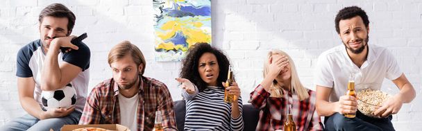 upset african american woman pointing with hand while watching football championship with sad multicultural friends, banner - Zdjęcie, obraz