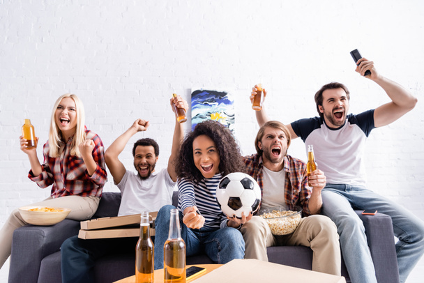podekscytowani wielonarodowymi przyjaciółmi pokazującymi gest wygranej podczas oglądania mistrzostw w piłce nożnej w domu - Zdjęcie, obraz