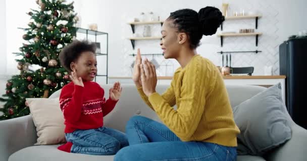 Portrét šťastný krásný Afroameričanka hrát s malým dítětem, zatímco sedí na pohovce v vánoční zdobené místnosti Boční pohled na milující maminku a dítě trávit čas spolu Dovolená koncept - Záběry, video
