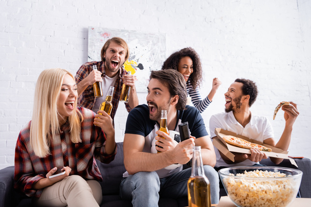 podekscytowani fani sportu trzymający butelki piwa podczas oglądania zawodów w domu - Zdjęcie, obraz