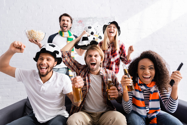 взволнованные мультиэтнические друзья, показывающие победный жест во время просмотра чемпионата по футболу дома - Фото, изображение