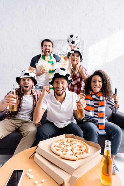 excited man showing win gesture while watching football championship with multiethnic friends - Photo, Image
