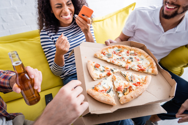 Afrika kökenli Amerikalı bir kadının yanında pizza tutan çok kültürlü arkadaşlar bulanık arka planda gülüyorlar. - Fotoğraf, Görsel