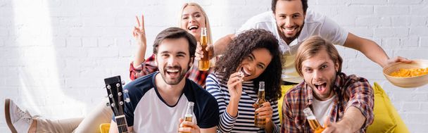 smiling woman showing victory gesture near excited friends holding beer during party, banner - 写真・画像