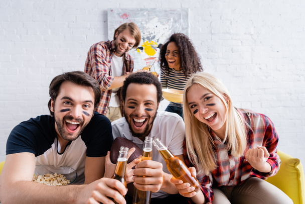 vidám multikulturális rögbi rajongók festett arccal koccintás üveg sört barátok közelében elmosódott háttér - Fotó, kép
