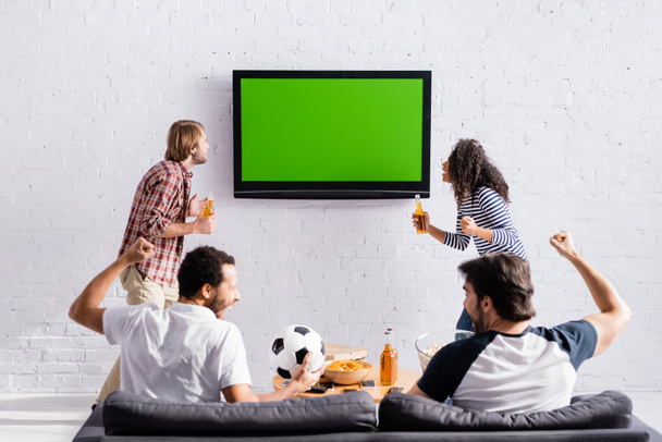 excited multicultural friends showing win gesture while watching football championship on tv - Фото, изображение