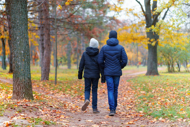 teen girl and boy walking through the park and enjoys autumn, beautiful nature with yellow leaves - Photo, Image