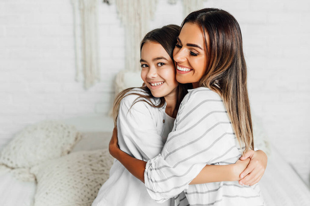 Daughter with mom happily smiling embracing on white room background. Happy childhood. - Foto, Imagem