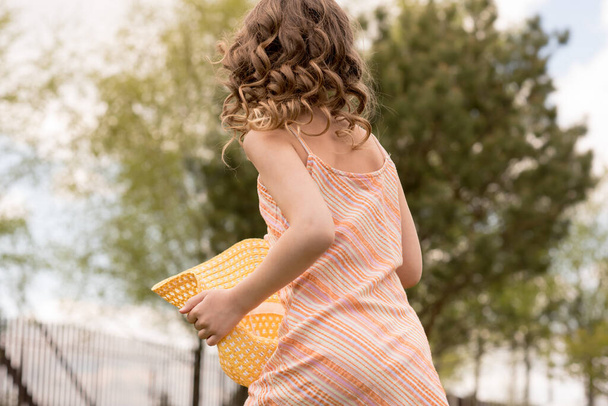 A little girl in a yellow dress with a hat runs in the summer in the country. The child runs a half-horse. Short shiny curly hair. The concept of children's power and fashion. Carefree childhood. - Fotoğraf, Görsel