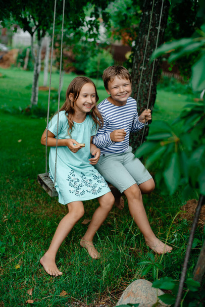 Boy and girl in summer ride on a swing in the park and laugh. The concept of sports and positive. Rest in the summer days. Copy space. Toning.  - Foto, Imagen