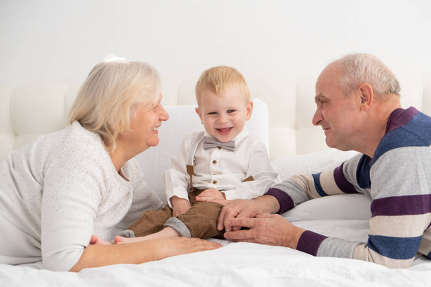 Glücklich gut aussehendes älteres Ehepaar mit ihrem entzückenden Enkel auf dem Bett.  - Foto, Bild