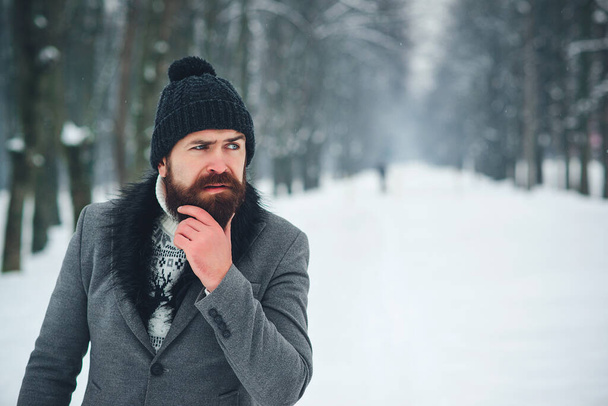 Young bearded man in stylish coat and black hat. Outdoor portrait of handsome man in winter outfit. Male winter fashion. Lifestyle, people and winter. - Fotó, kép