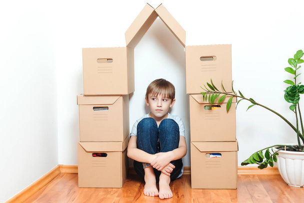 Szomorú gyerek, aki dobozokból bújkál a házban. Jelzálog, emberek, lakás, költözés és ingatlan. A gyerek új otthonról álmodik. Elfogadási koncepció. - Fotó, kép