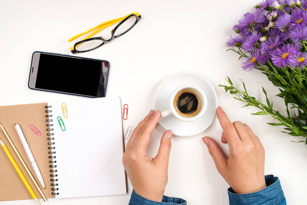 Woman's workplace with coffee, phone and flowers. Morning coffee cup, notebook, pencil, glasses and flowers on white table. Top view, flat lay. Planning and design concept. - Photo, Image