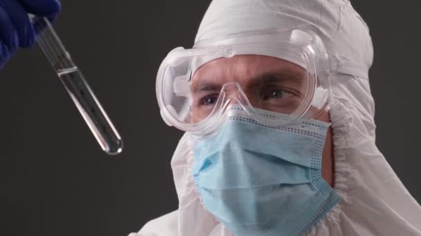 medico in una tuta protettiva medico tiene una fiala di vaccino coronavirus tra le mani e guardare nella fotocamera. Pandemia e vaccinazioni. Test di laboratorio. Ricerca clinica - Filmati, video