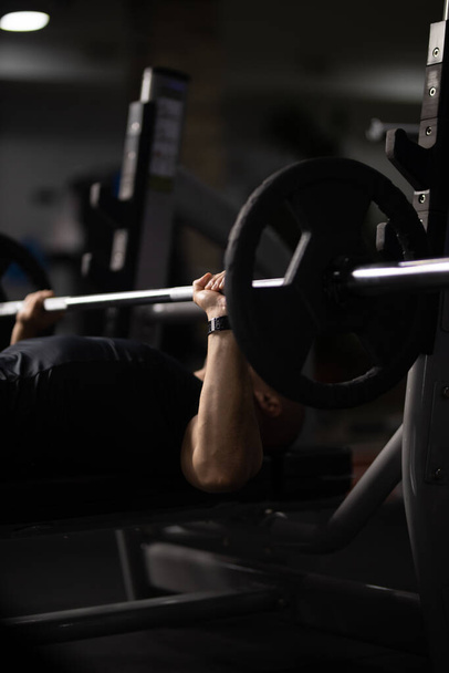 A vertical shot of a person lifting weights in a gym with a dark blurry background - Photo, image