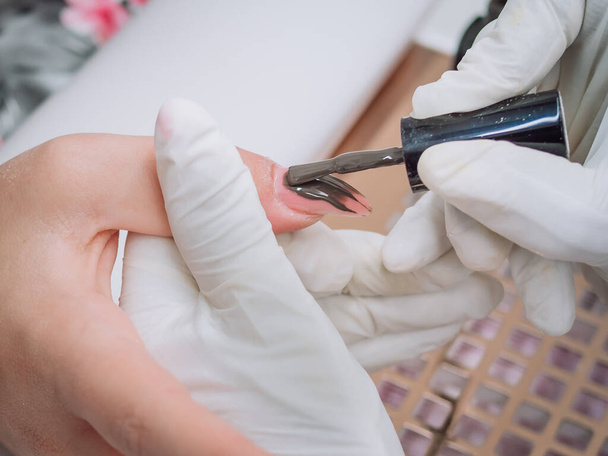 A professional esthetician applying permanent polish on the customers nails  - Foto, Imagem