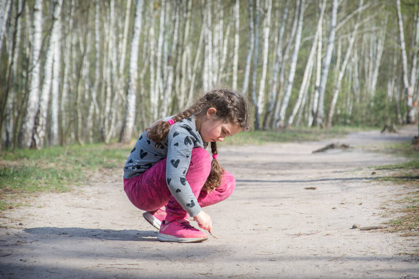 Влітку, в яскравий сонячний день у лісі на шляху, дівчина малює палицею
. - Фото, зображення