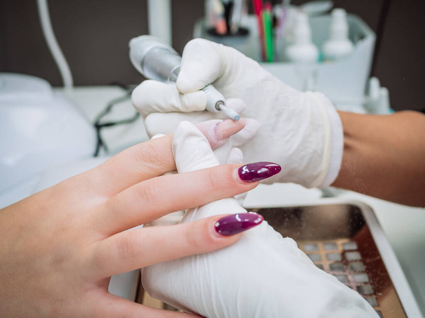 A professional esthetician using an electric nail file drill to remove acrylic gel from nails - Foto, Imagen