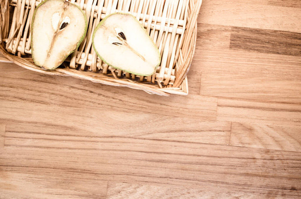 A high angle shot of a half-cut pear on a basket on a wooden surface - Fotó, kép