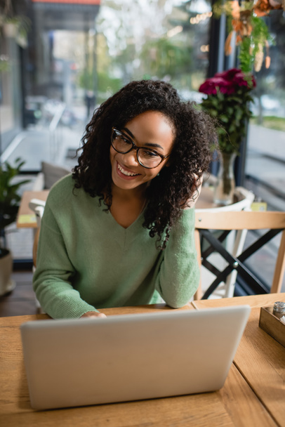 mulher americana africana feliz em óculos olhando para laptop no café  - Foto, Imagem