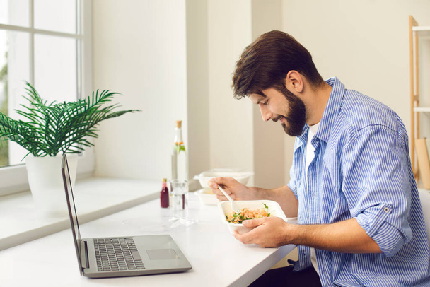 Busy young man eating takeaway food during lunch break at home or in the office - Foto, Imagen