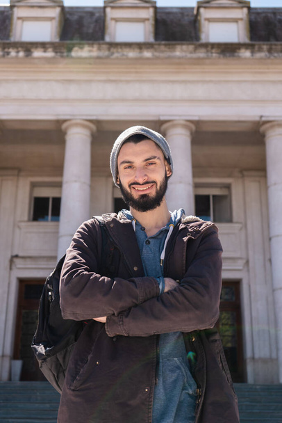 Άνδρας φοιτητής χαμογελά, στέκεται μπροστά από το κτίριο του πανεπιστημίου. Κάθετη βολή. - Φωτογραφία, εικόνα