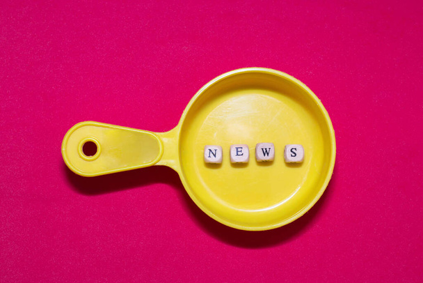 Phrase news from wooden letters on a plastic toy frying pan, red background. News preparation concept. - 写真・画像