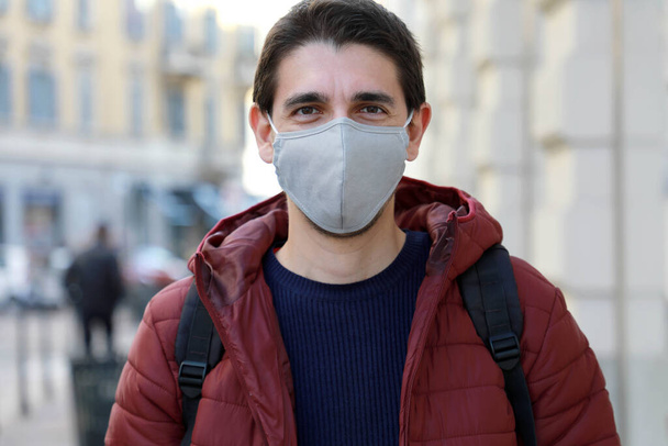 Portret van een jonge man met gezichtsmasker staat op straat en kijkt naar de camera - Foto, afbeelding