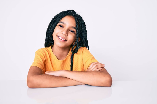 Nuori afrikkalainen amerikkalainen tyttö lapsi punokset yllään rento keltainen t paita onnellinen kasvot hymyillen ristissä kädet katsoen kameraan. positiivinen henkilö.  - Valokuva, kuva