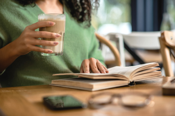 Kafe 'de kitap okurken elinde latte olan Afro-Amerikan kadın manzarası. - Fotoğraf, Görsel