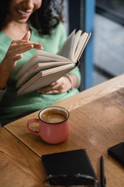 vista ritagliata della donna afro-americana sfogliando le pagine del libro nel caffè - Foto, immagini