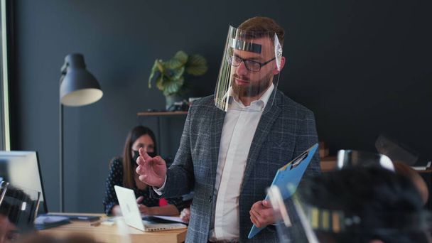 Successful serious young Caucasian coach businessman speaking at office meeting wearing COVID-19 safety face shield. - Foto, Imagem