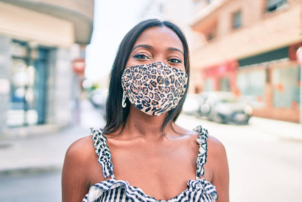 Young african american woman wearing coronavirus protection mask walking at street of city - Photo, image