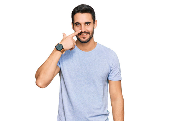 Young hispanic man wearing casual clothes pointing with hand finger to face and nose, smiling cheerful. beauty concept  - Photo, image
