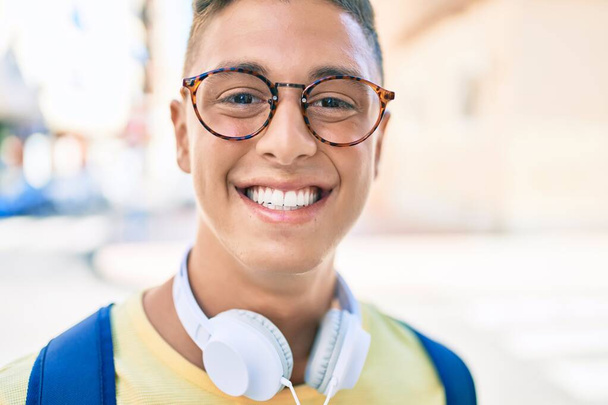 Joven estudiante hispano sonriendo feliz usando auriculares caminando en la calle de la ciudad - Foto, imagen