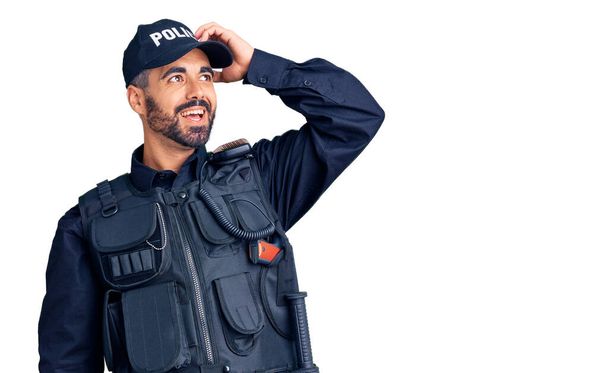 Junger hispanischer Mann in Polizeiuniform lächelt selbstbewusst und berührt die Haare mit erhobener Hand, posiert attraktiv und modisch  - Foto, Bild