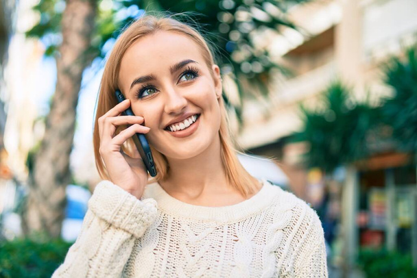 Young blonde girl smiling happy talking on the smartphone at the city. - Photo, Image