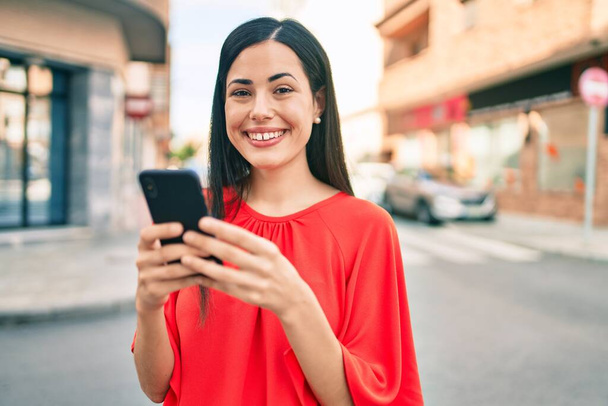 Joven chica latina sonriendo feliz usando smartphone en la ciudad. - Foto, Imagen