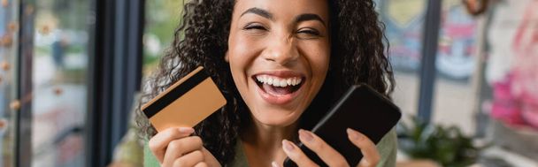 iloinen afrikkalainen amerikkalainen nainen nauraa pitäen älypuhelin ja luottokortti, banneri - Valokuva, kuva