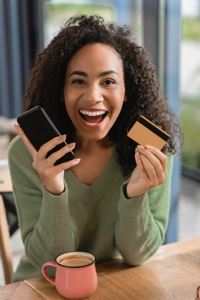 excitée femme afro-américaine tenant smartphone et carte de crédit - Photo, image